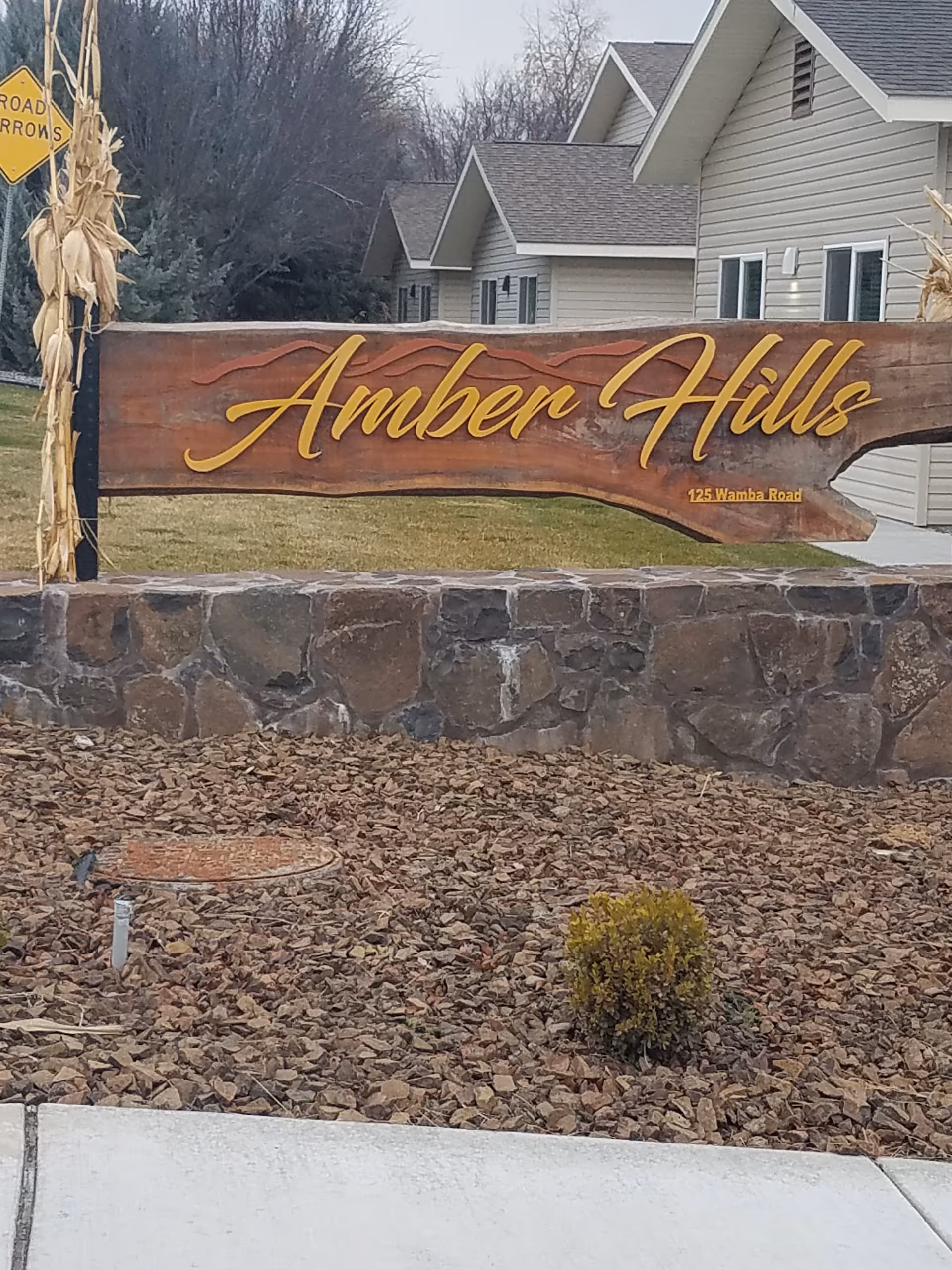 Wooden Amber Hills sign on stone wall with beige buildings behind