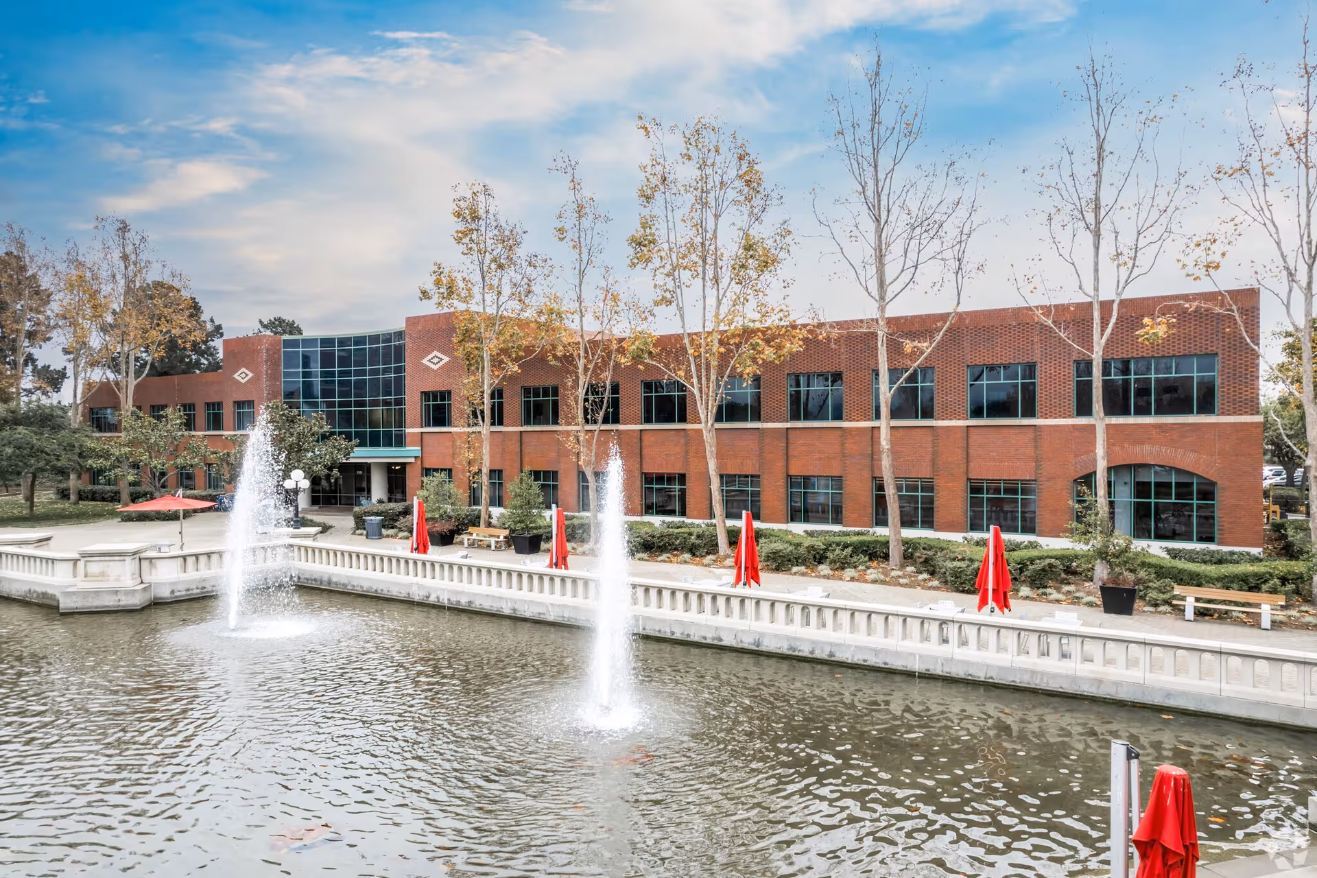 Brick senior living facility with a pond, fountains, trees, and outdoor seating.