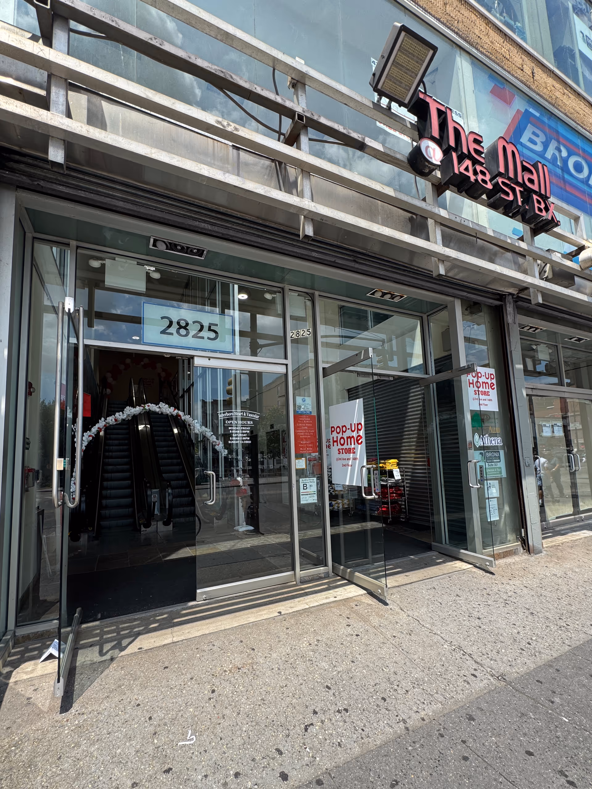 Glass storefront entrance of a mall with escalator visible inside and signage.