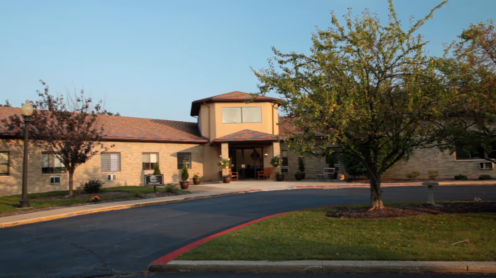Exterior view of East Park Living facility showing a single-story building with a central entrance, surrounded by trees and a curved driveway.