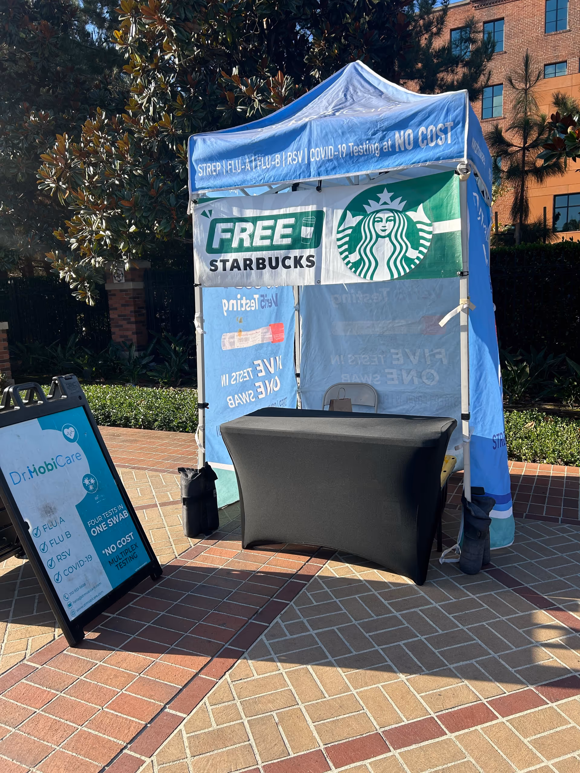 Blue outdoor tent with Free Starbucks signage and a black table on brick pavement.