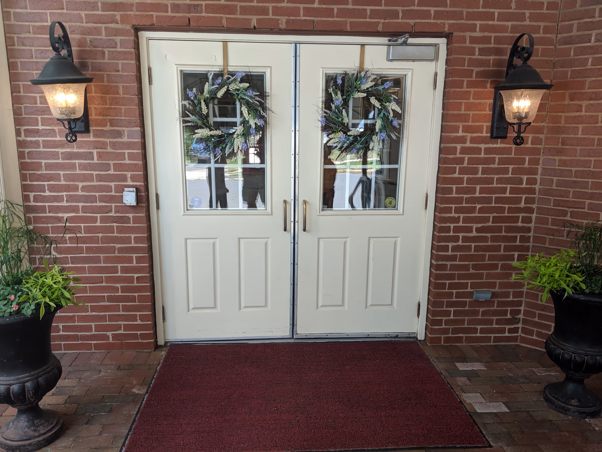 Double white doors with wreaths on a brick entrance flanked by lantern lights.