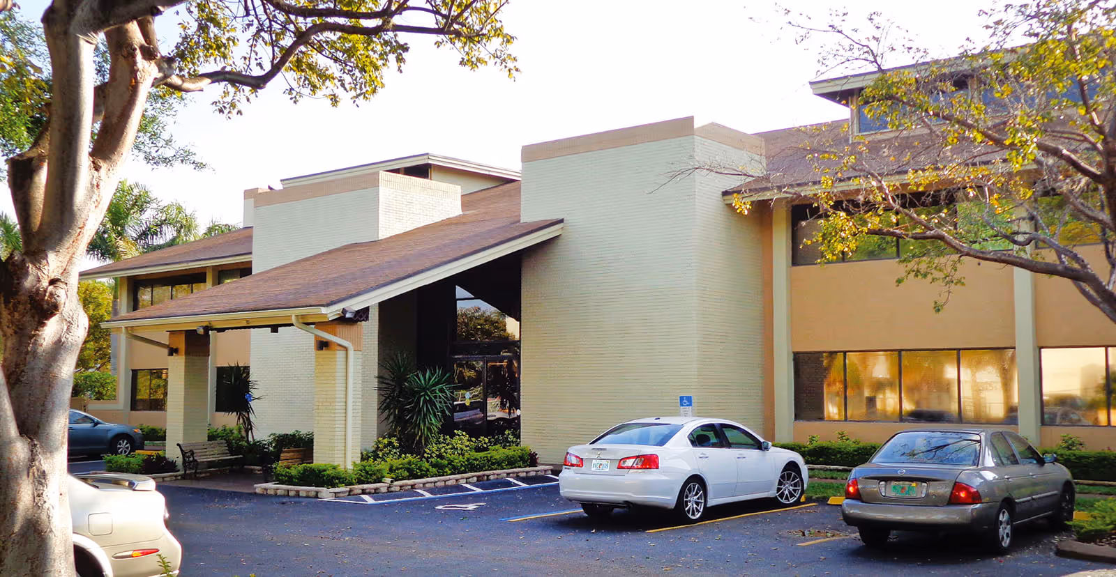 Exterior front of a two-story assisted living building with a covered entrance and several cars parked in the lot.