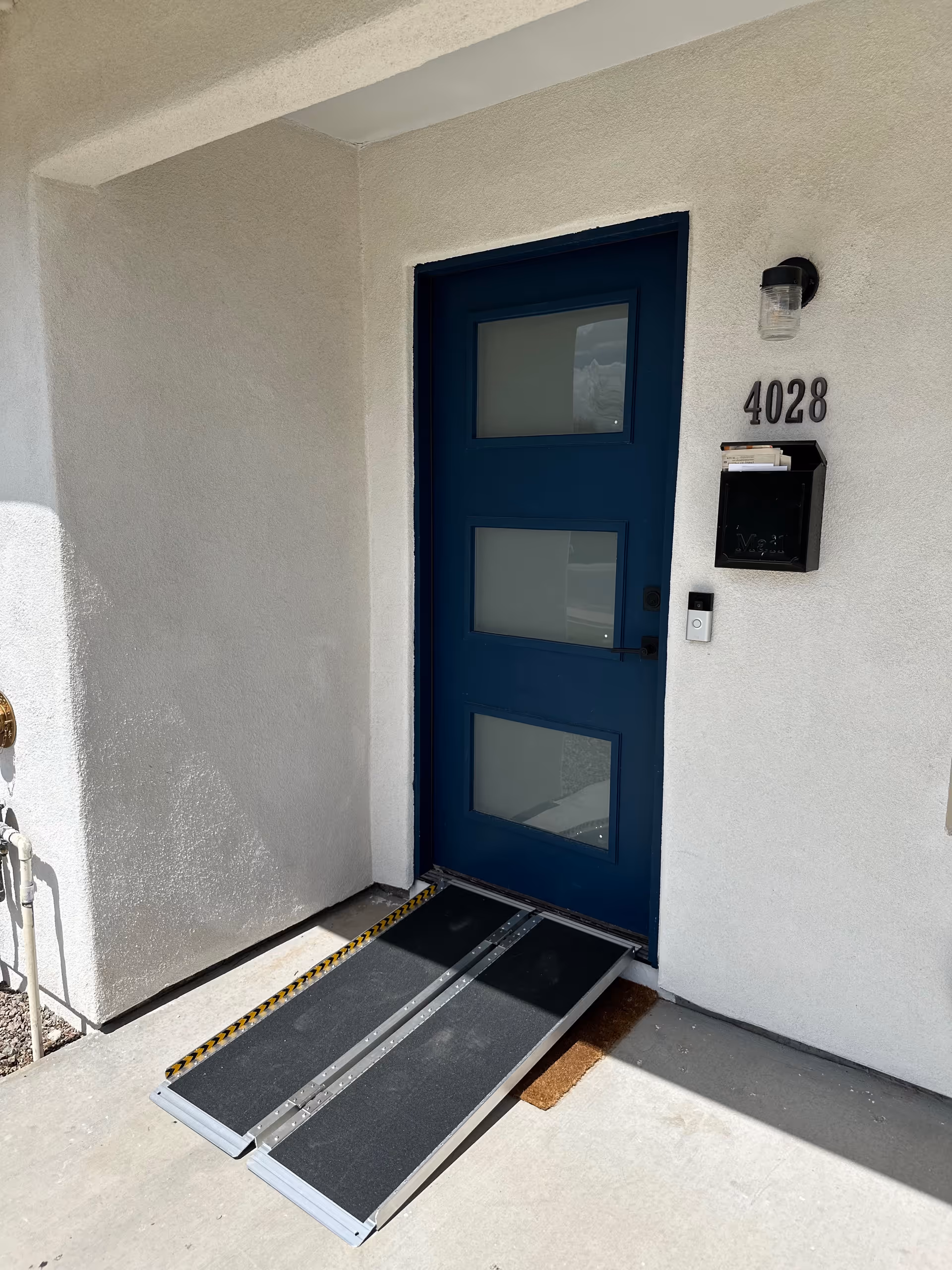 Blue front door with a ramp into a white exterior building.