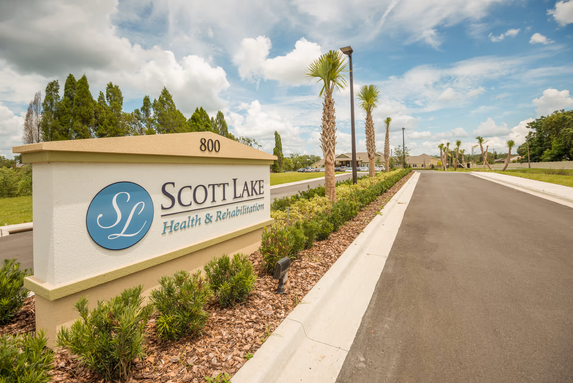 Entrance sign for Scott Lake Health & Rehabilitation with landscaped curb and palm trees.