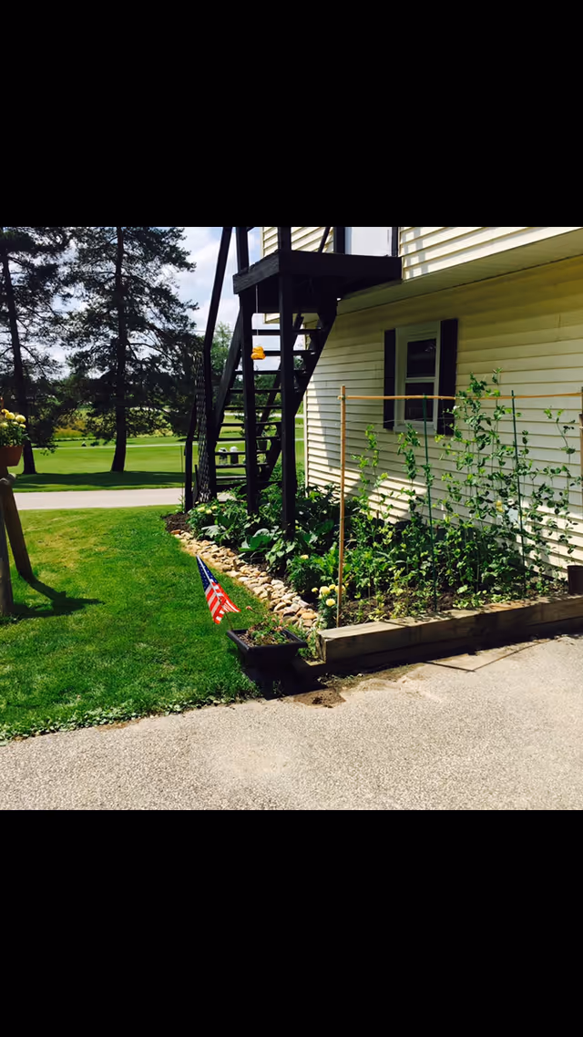 Exterior of light-colored building with stairs, garden bed, and American flag.