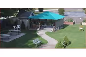 An outdoor courtyard with a teal canopy, benches, and a curved sidewalk beside a small pavilion.