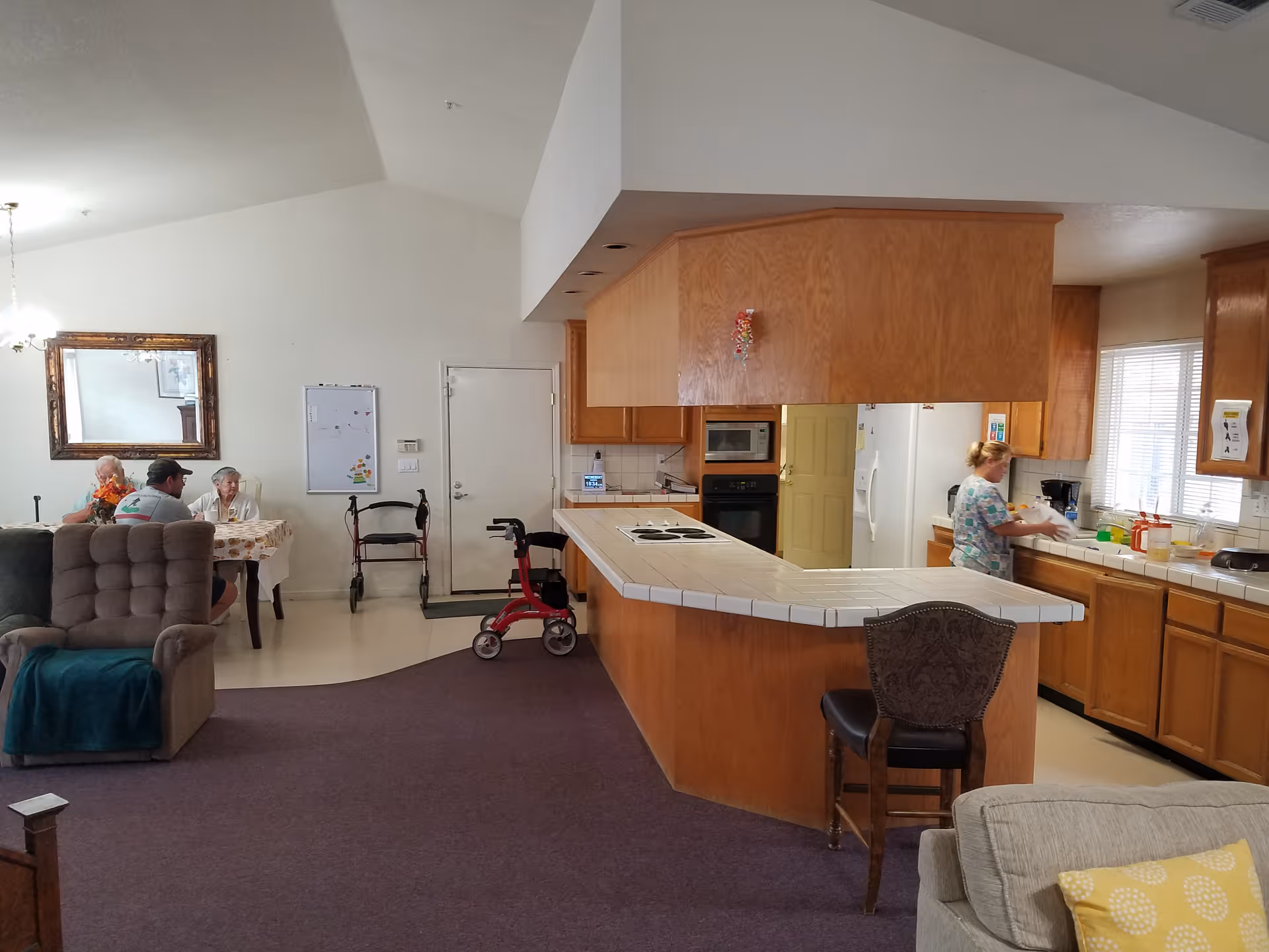 Spacious senior living common area featuring a large kitchen island and residents seated nearby.
