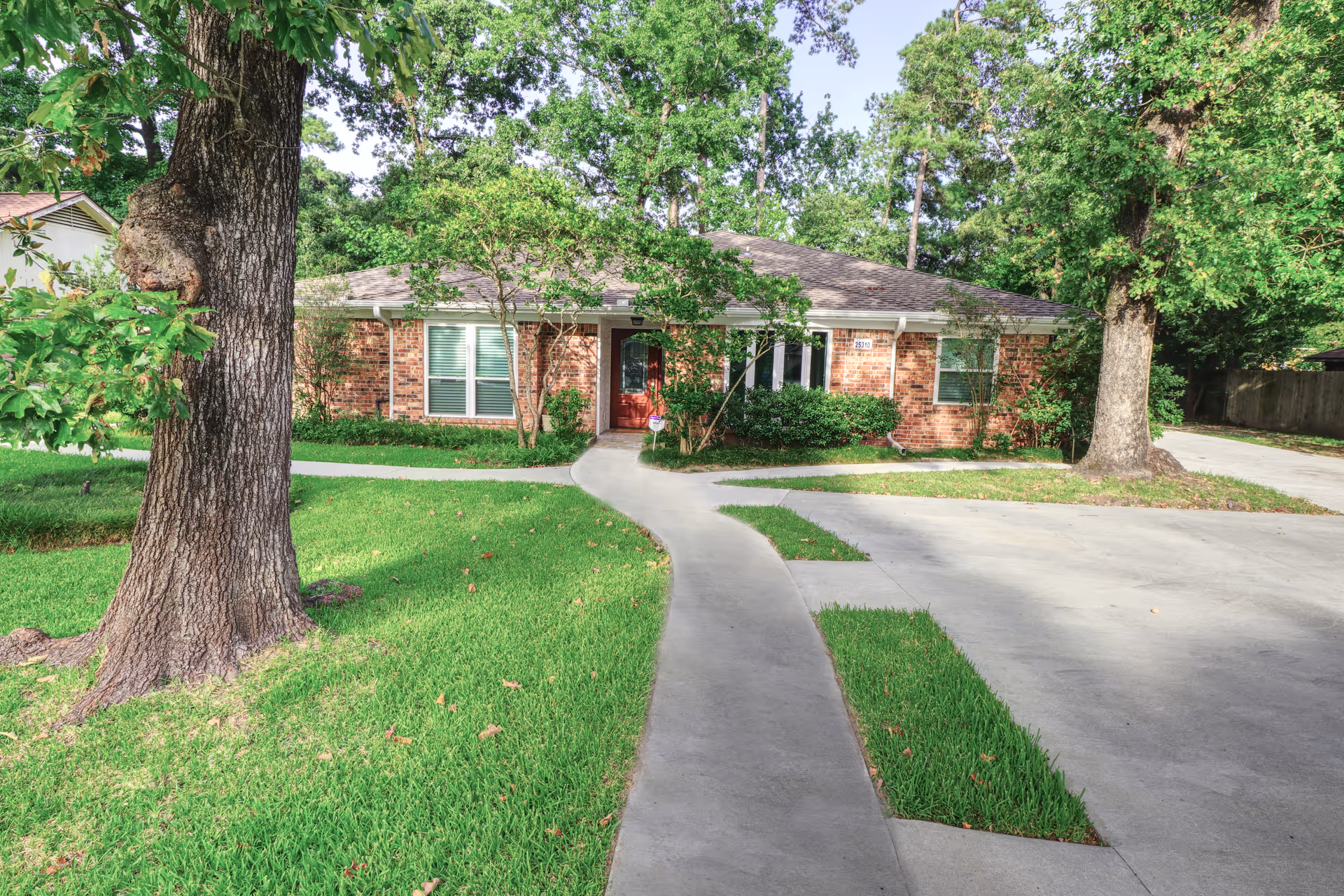 Front exterior of a single-story brick building with a walkway and driveway flanked by large trees and a well-kept lawn.