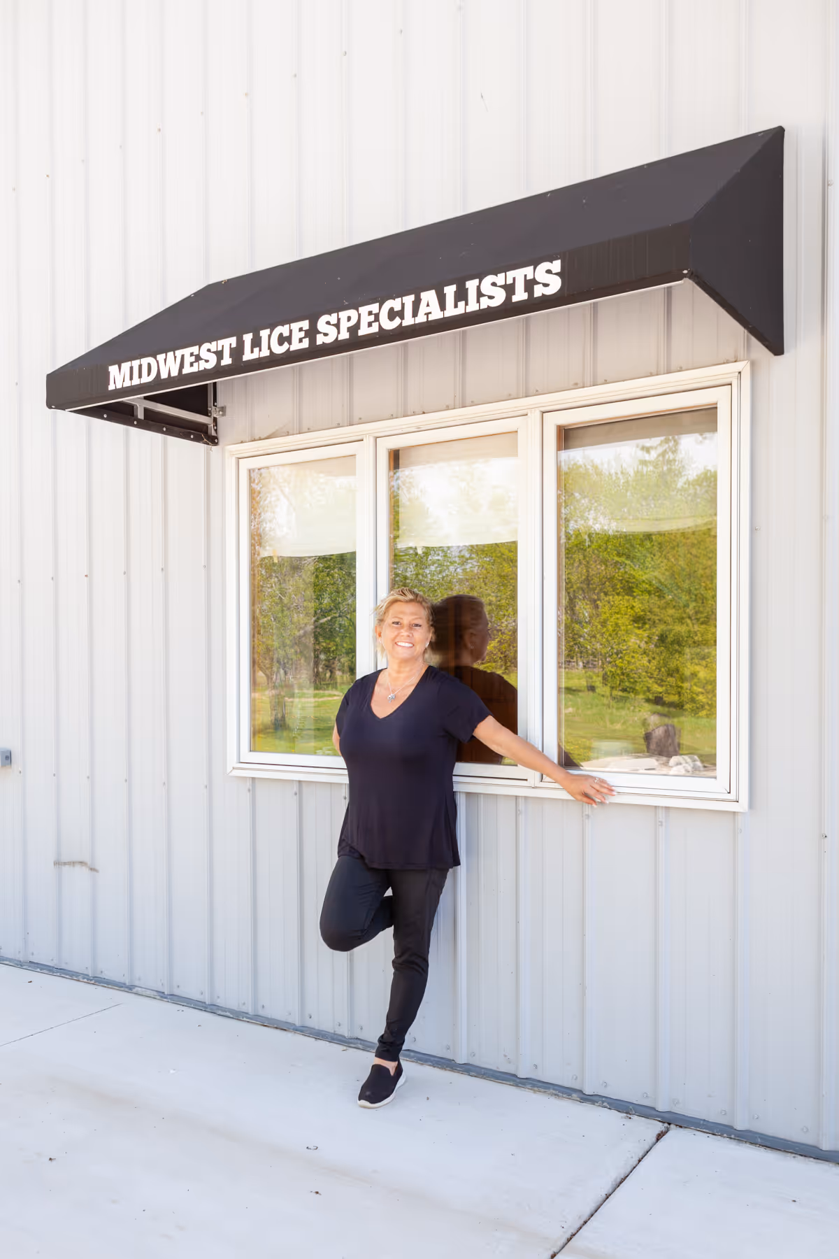 A woman stands outside a building with a black awning reading Midwest Lice Specialists.