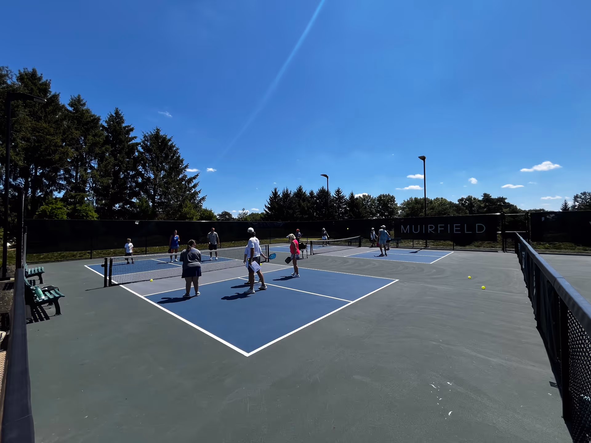 Outdoor tennis court with several players under a clear blue sky.