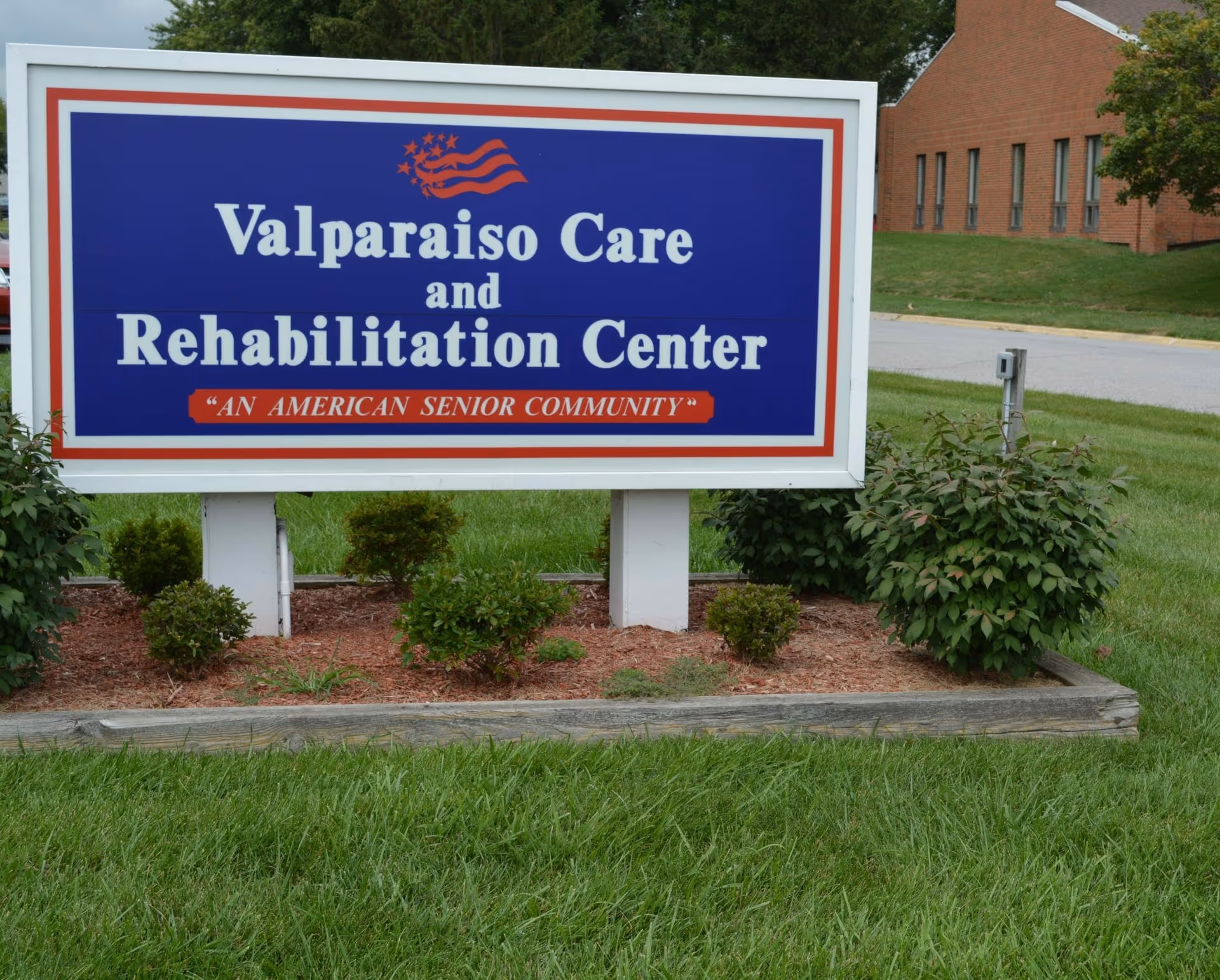 Large blue sign on a lawn that reads 'Valparaiso Care and Rehabilitation Center' in front of a brick building.