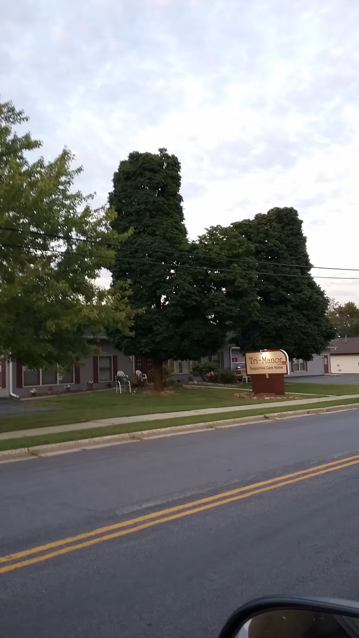 Exterior view of Tri-Manor Ltd facility with sign, trees, and street.