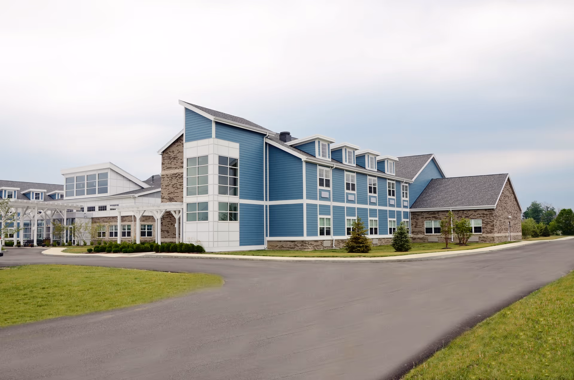 Exterior view of a blue and gray senior living campus building beside a curved road.