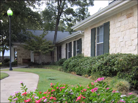 Senior living facility exterior with stone walls, hedges, and a curved walkway