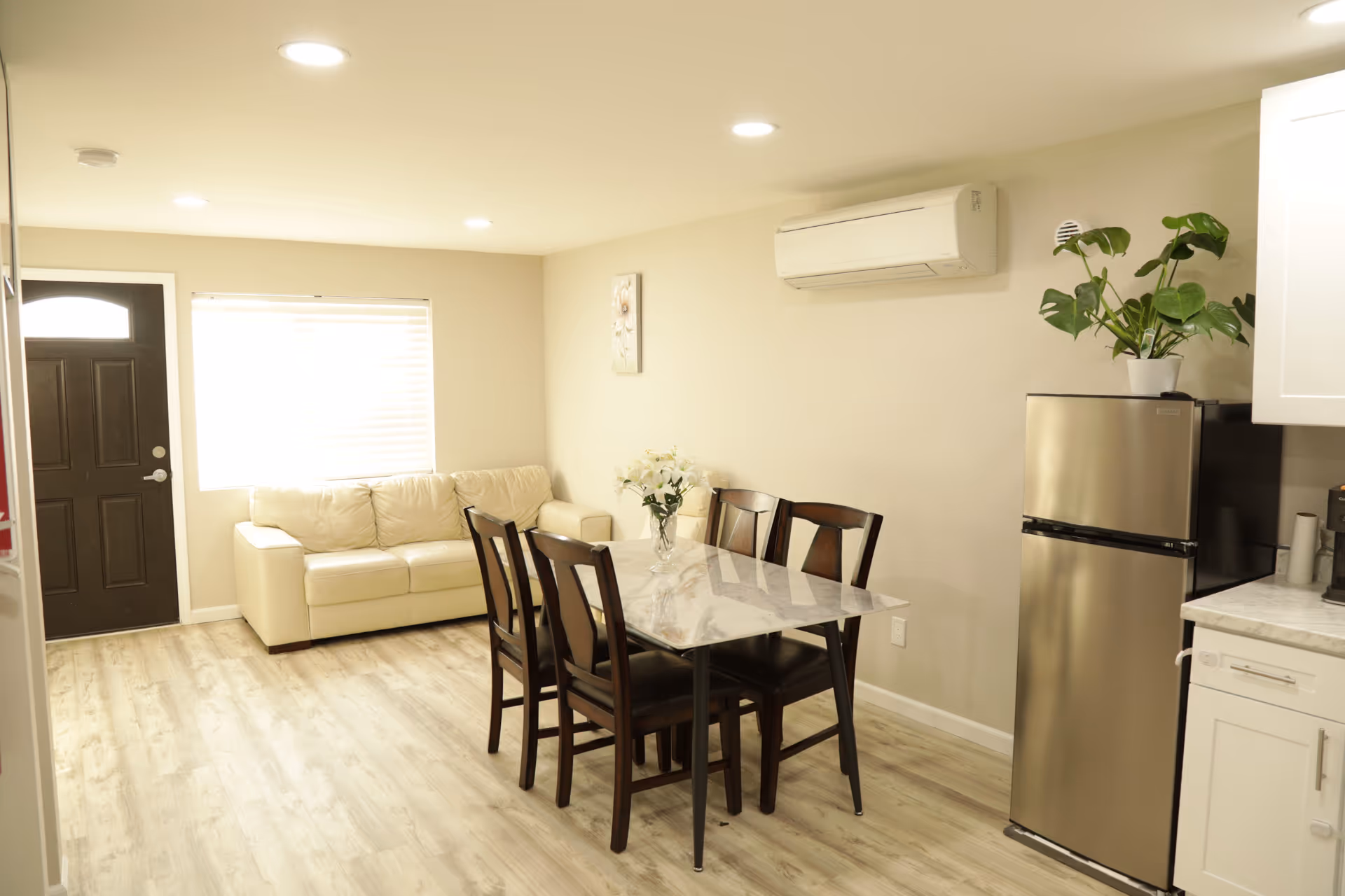 Bright open dining area with a marble table, dark chairs, a beige sofa, and stainless fridge.