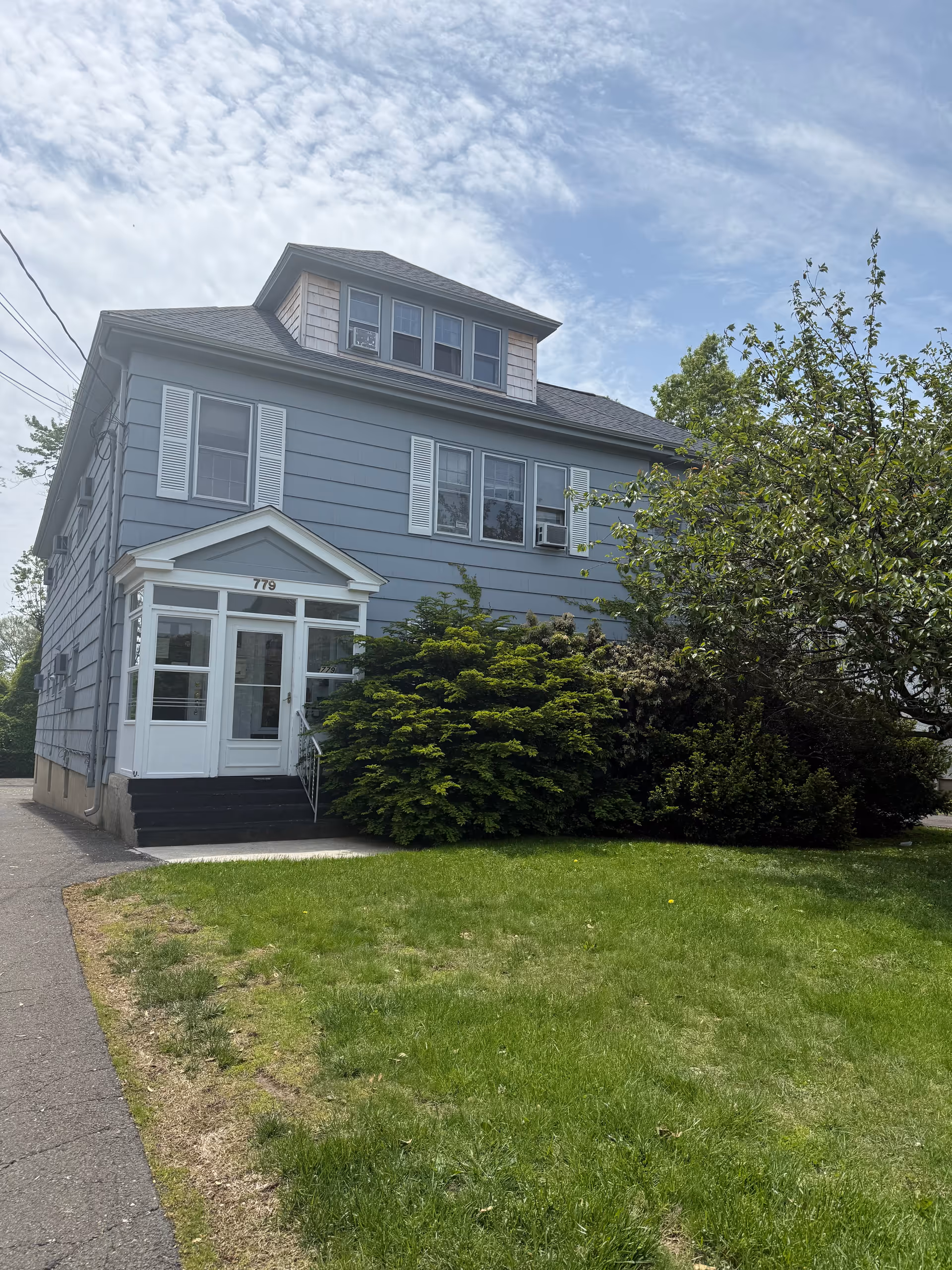 Blue two-story house with white trim and a front entrance, surrounded by lawn.