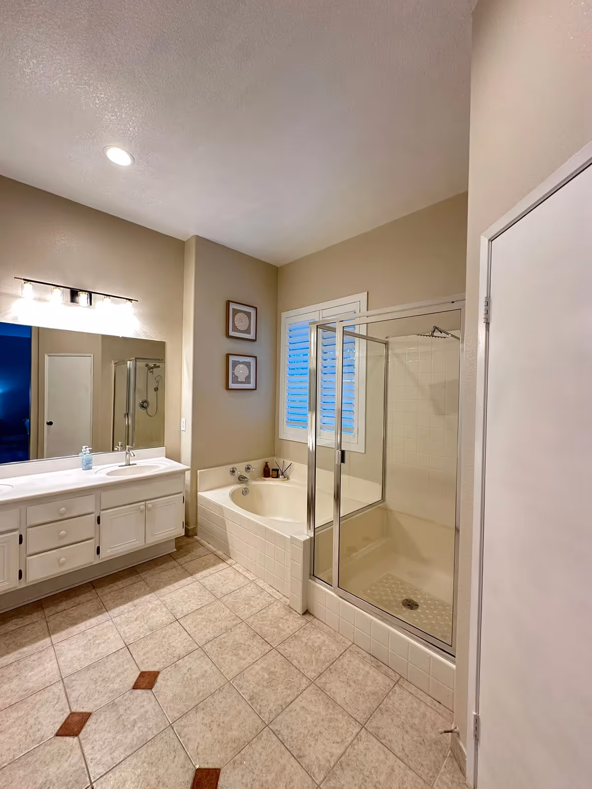 Bright bathroom with double vanity, bathtub, and glass enclosed shower in a senior living facility.