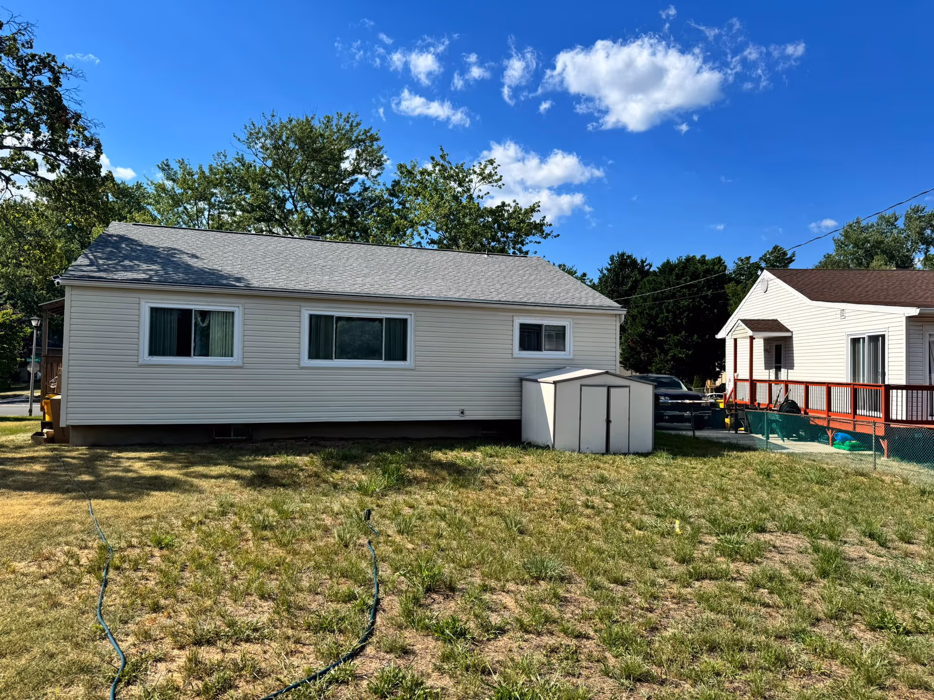 Single-story beige mobile home in a grassy yard with a shed and neighboring house.