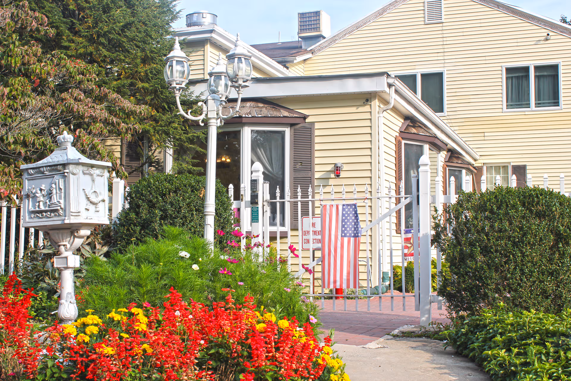 Front view of The Country Home facility with a gated entrance, garden, and American flag.