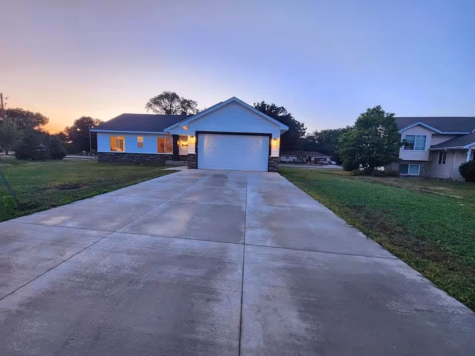 Wide concrete driveway leads to a single-story facility with a two-car garage at dusk.
