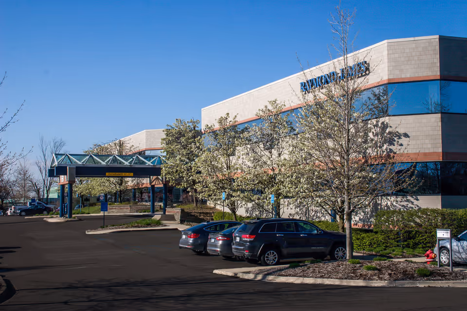 Exterior view of a Raymond James building with a parking lot and trees.