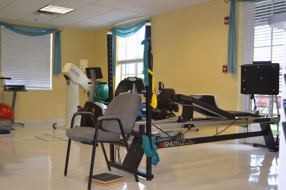 Indoor rehabilitation gym with treadmill, exercise equipment, a chair, and blue-curtained windows.
