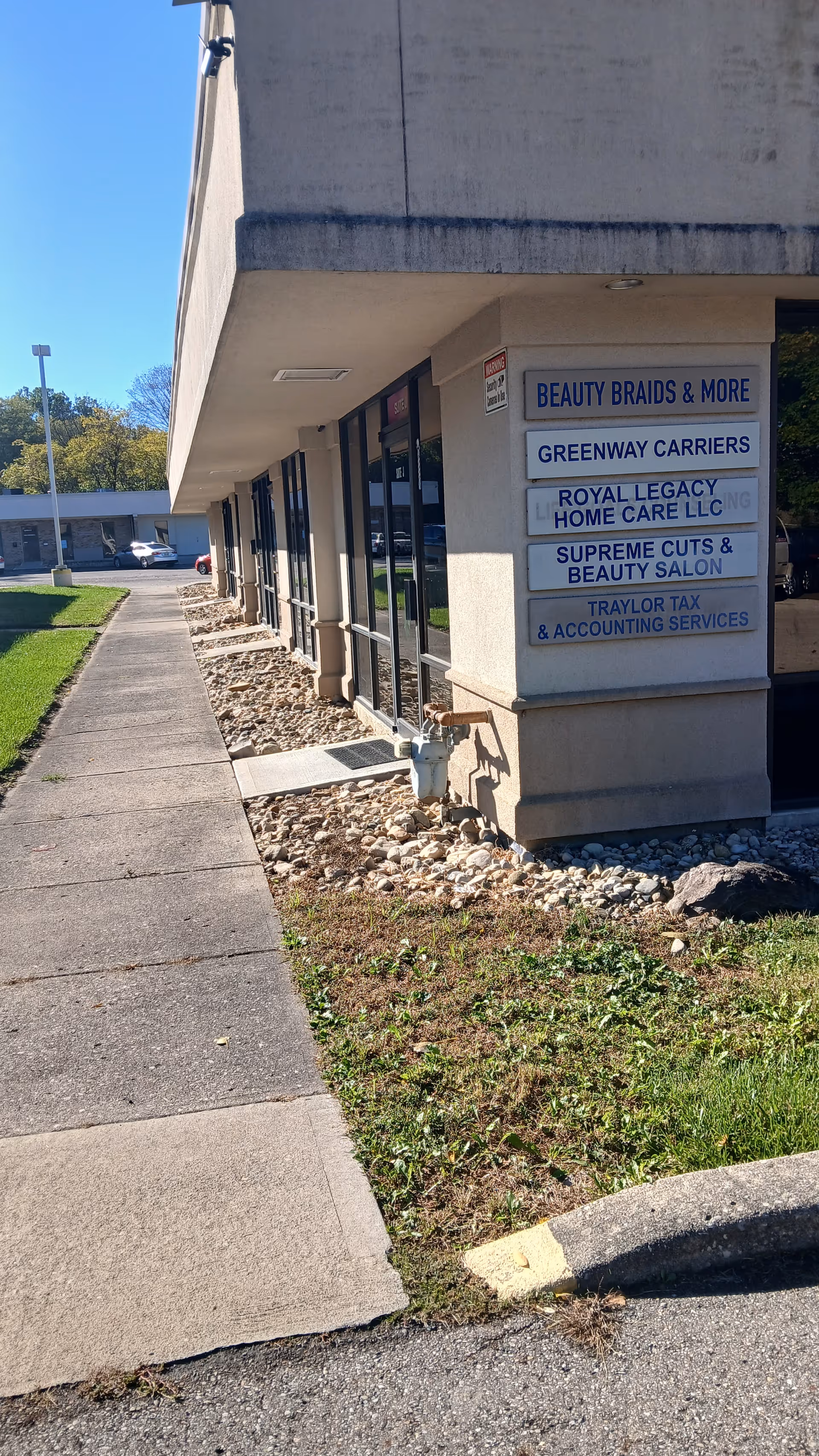 Exterior of a beige commercial building with signs for Royal Legacy Home Care LLC and salons.
