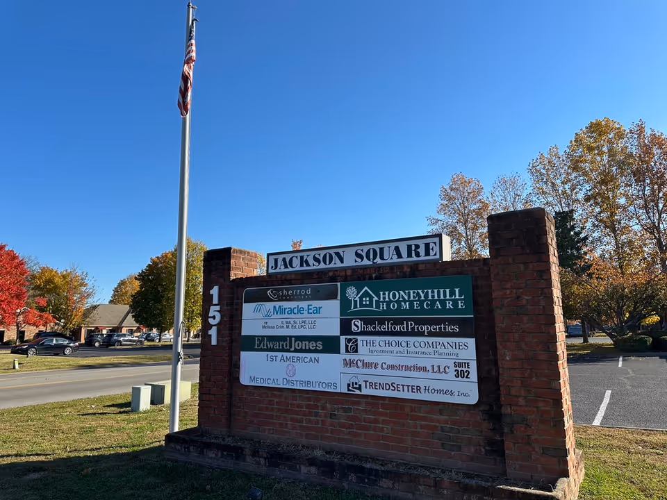Brick sign reading Jackson Square with HoneyHill HomeCare logo, flagpole, and fall trees.