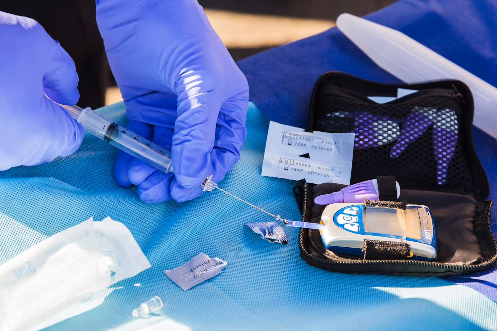 Gloved hands prepare a syringe beside a medical device on a blue tray.