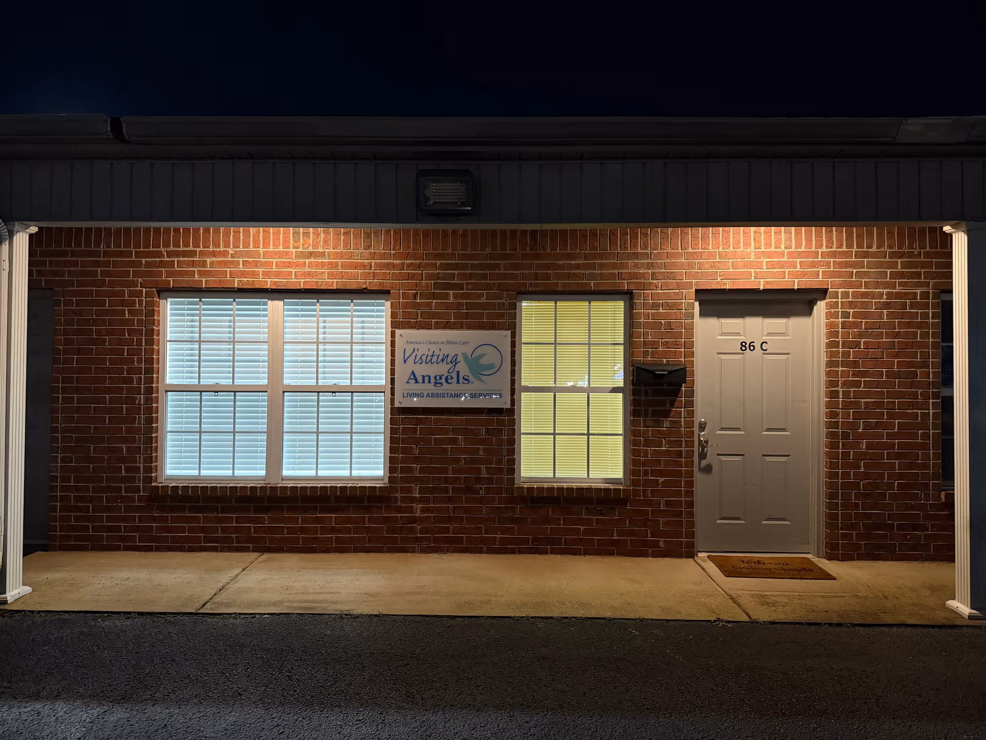 Brick facility exterior with two windows, a door, and a Visiting Angels sign.