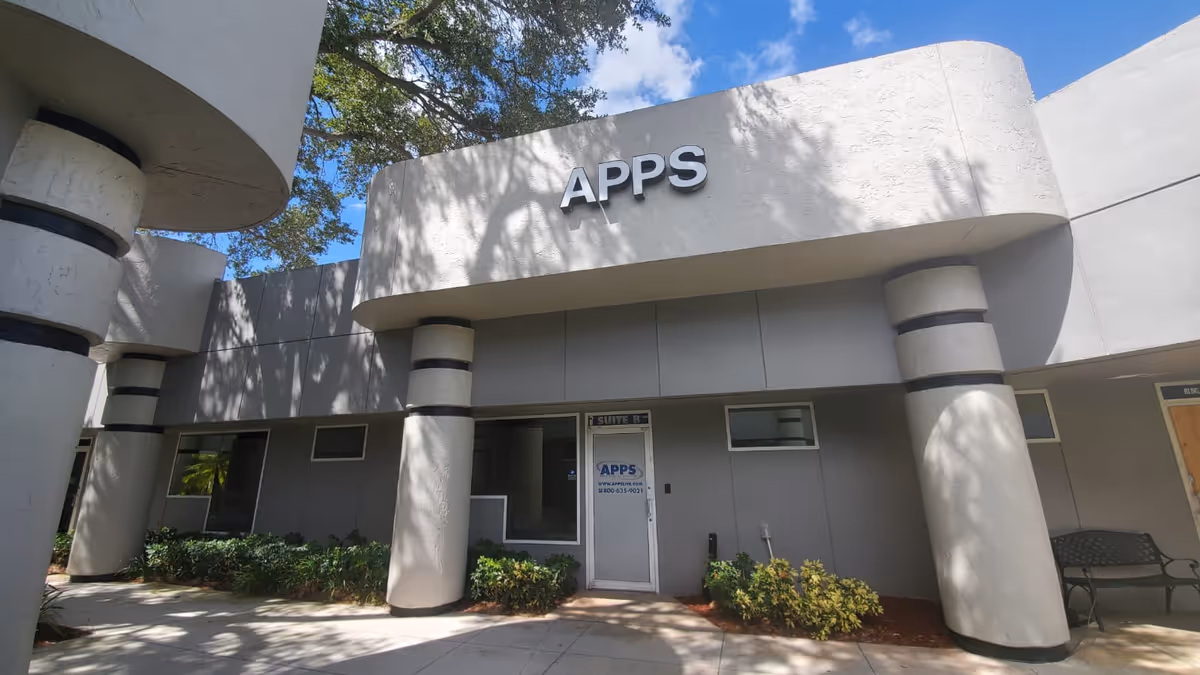 Gray modern building front with APPS sign and entrance door under curved canopy.