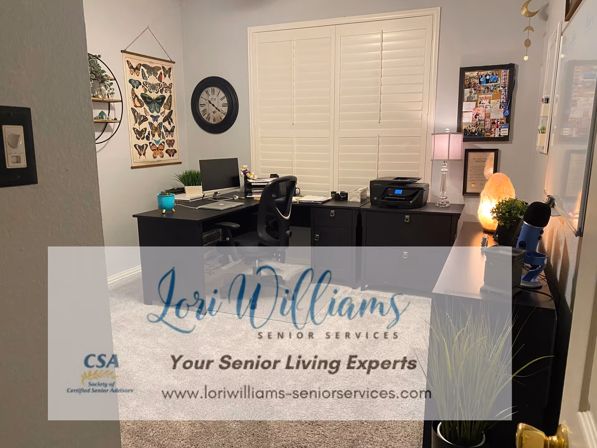 Home office setup with desk, computer, printer, butterfly art, clock, and logo watermark.