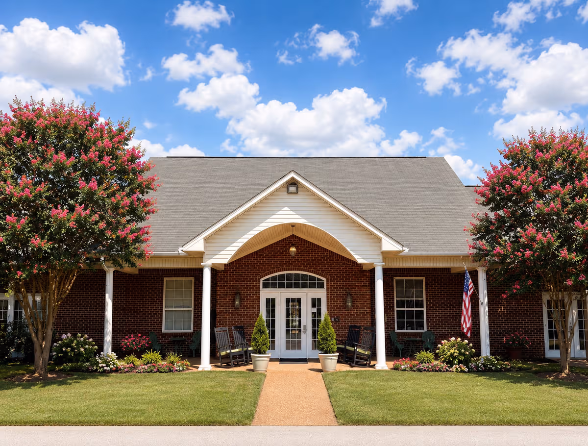 Heritage Assisted Living building with brick exterior, arched entrance, and flowering trees lining walkway.