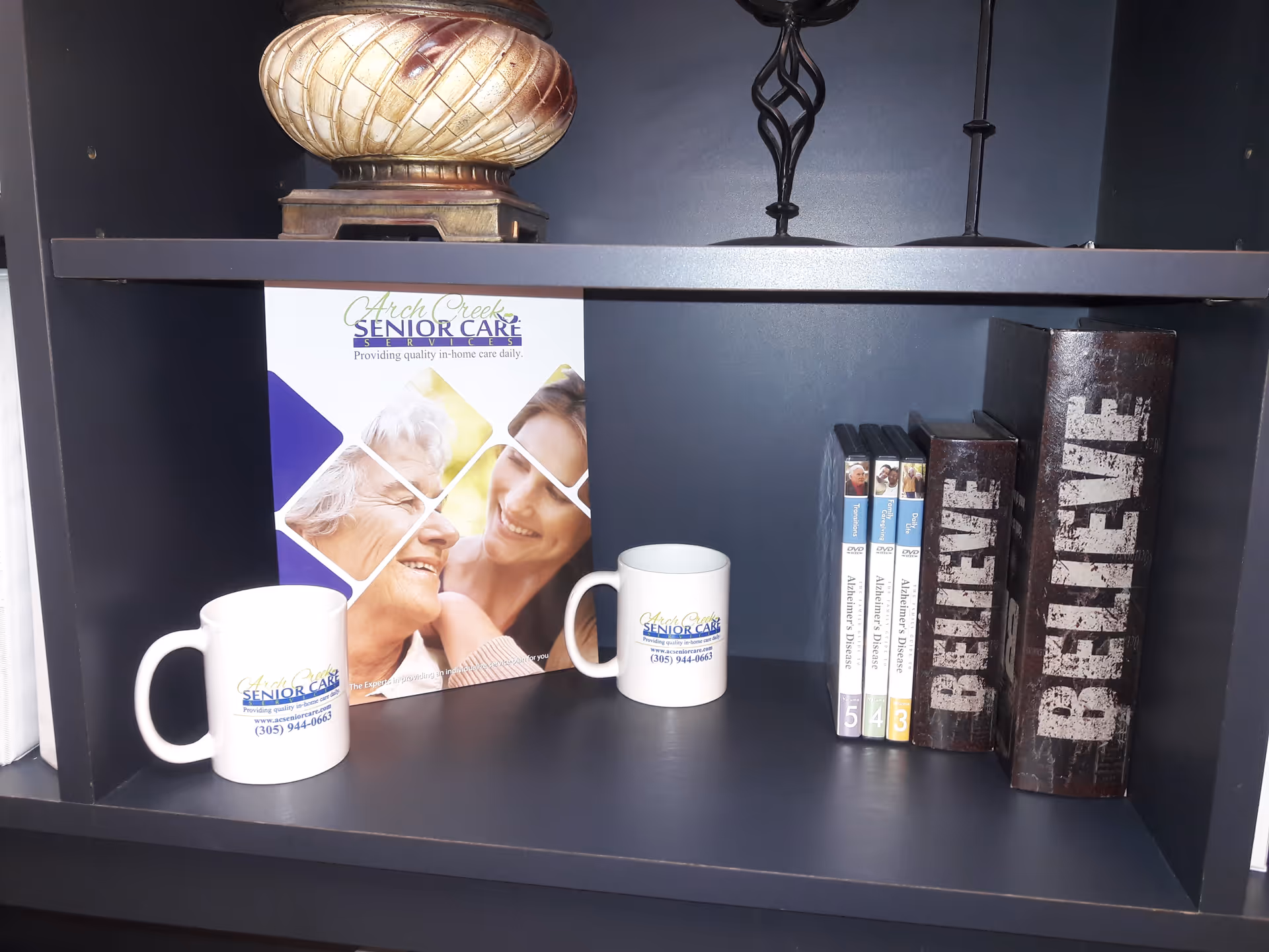 Arch Creek Senior Care promotional brochure and branded mugs arranged on a dark shelf.