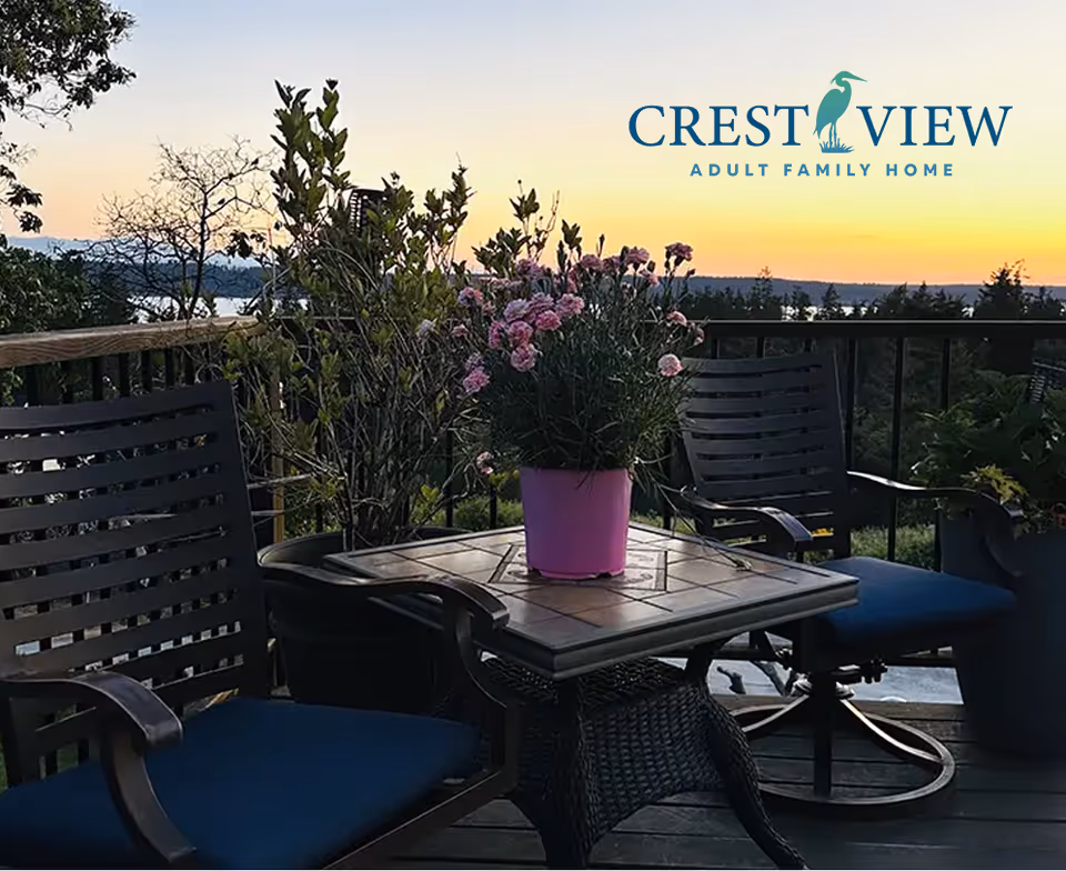 Outdoor balcony with chairs, table, and pink potted flowers at sunset, Crest View logo.