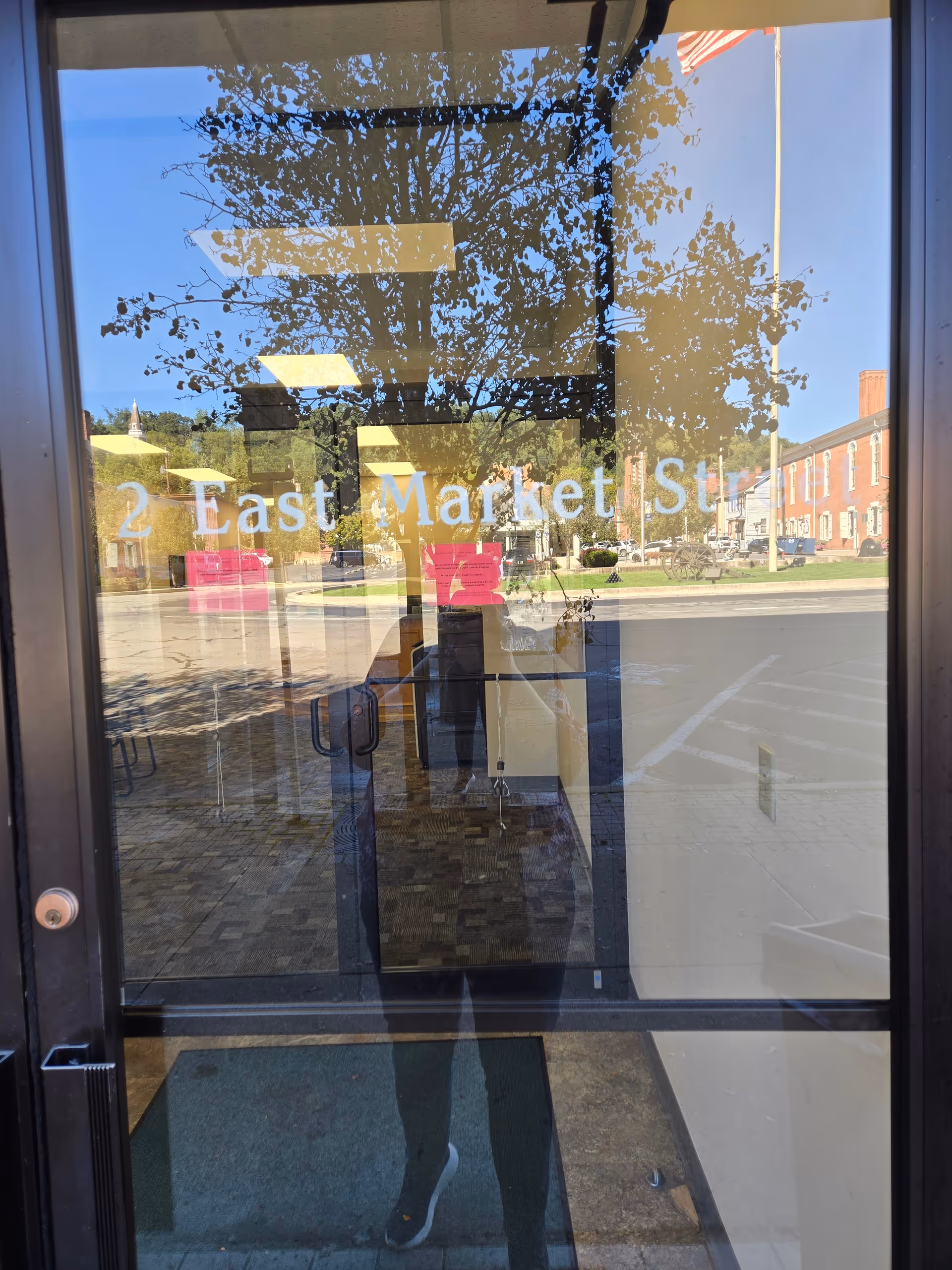 Glass entry door reflecting street view and trees, with '2 East Market St' signage.