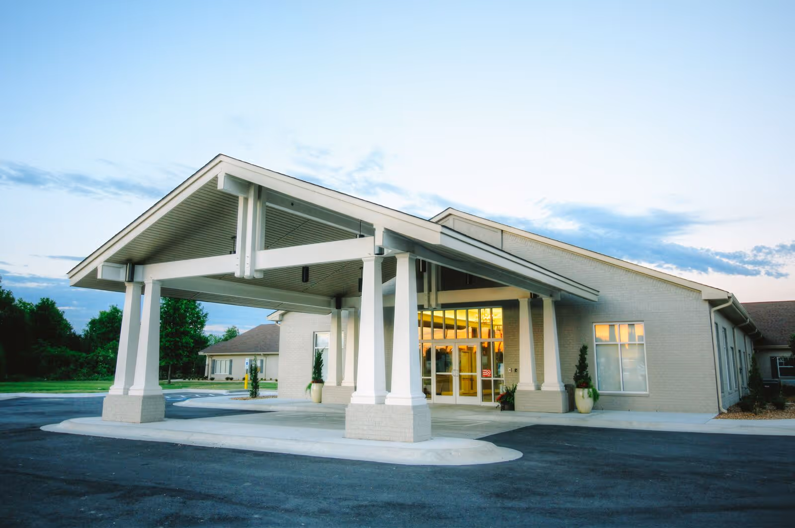 Front entrance of a single-story senior living facility with a covered drop-off porte-cochère and glass doors.