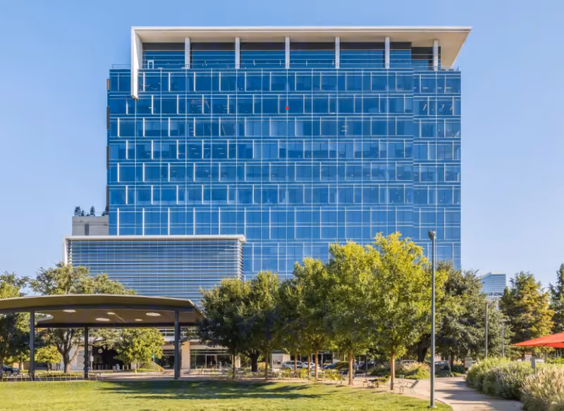 Exterior view of a modern glass building with trees and a walkway.