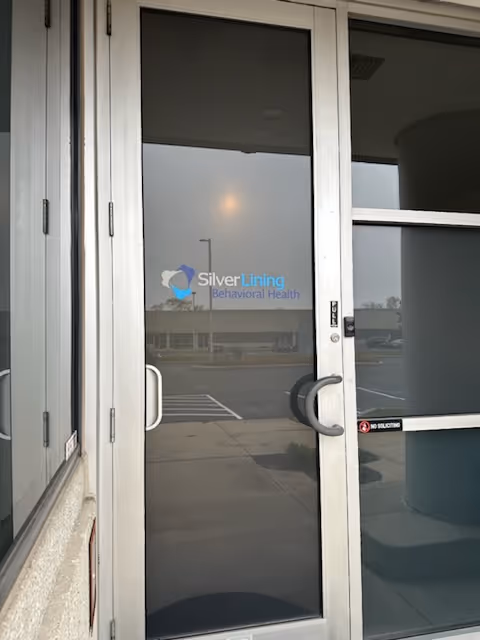 Glass entrance door with the Silver Lining Behavioral Health logo, reflecting a parking lot.