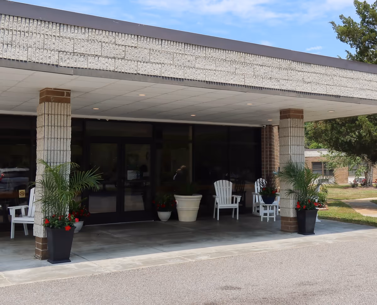 Exterior entrance of Southport Health and Rehabilitation Center with planters, chairs, and glass doors.