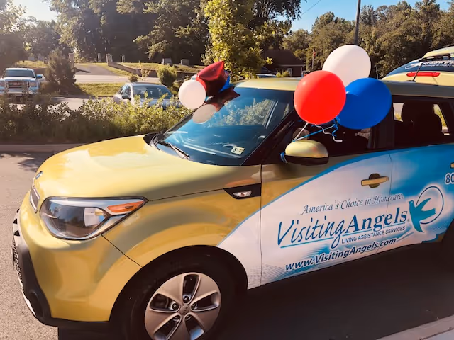 Yellow and white Visiting Angels van decorated with balloons in a parking lot.