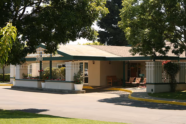 Exterior view of a Primrose Alzheimer's Living entrance with chairs and potted plants.