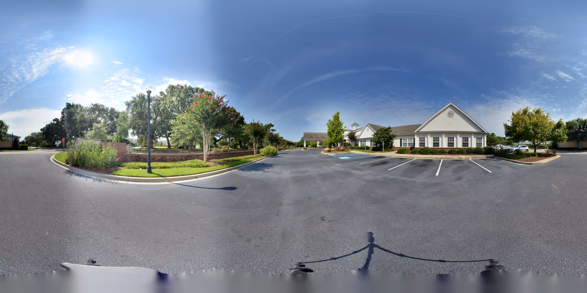 Parking lot and landscaped entrance in front of a single-story white senior living building under a clear blue sky.
