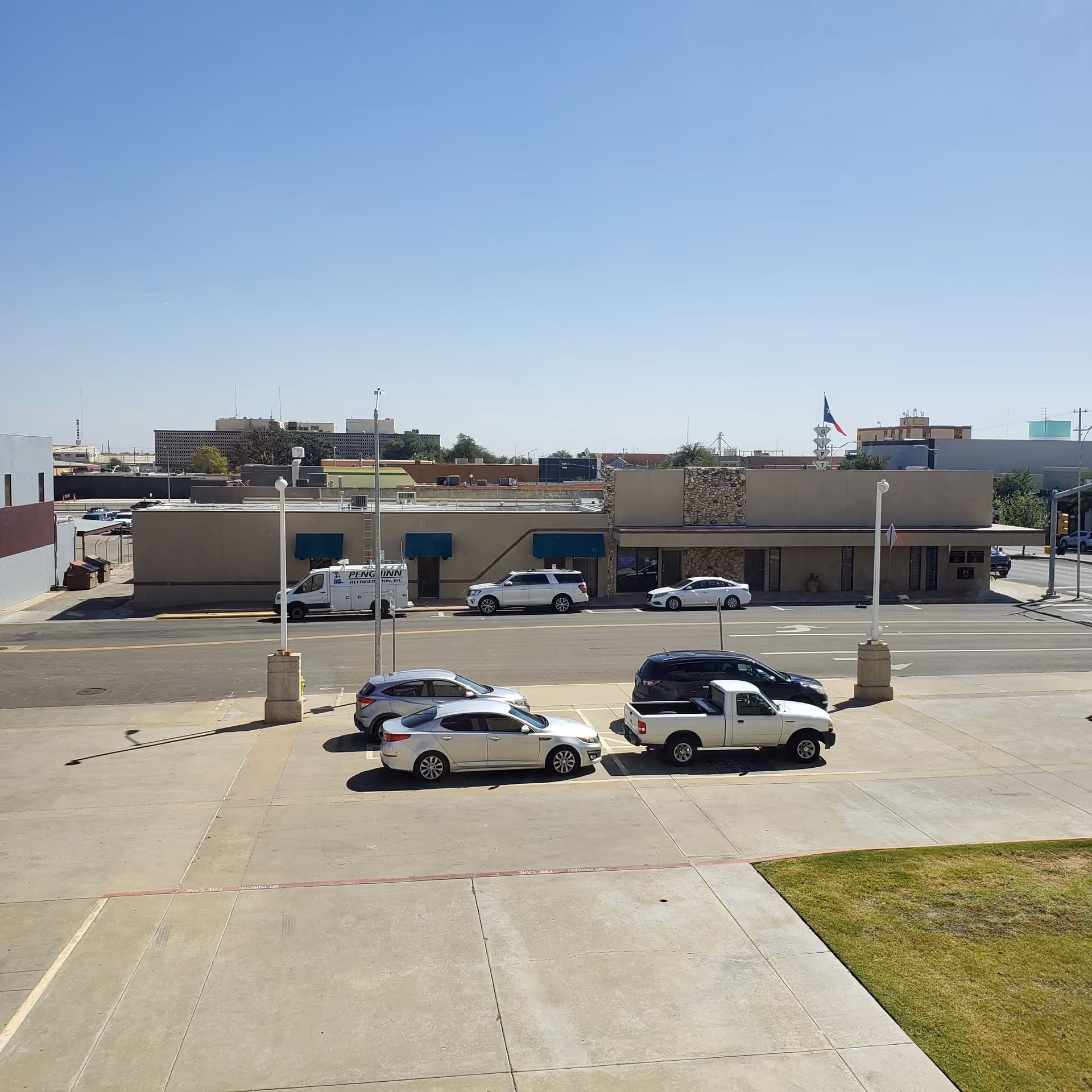 Exterior view of a single-story building with cars parked in front and a flag.