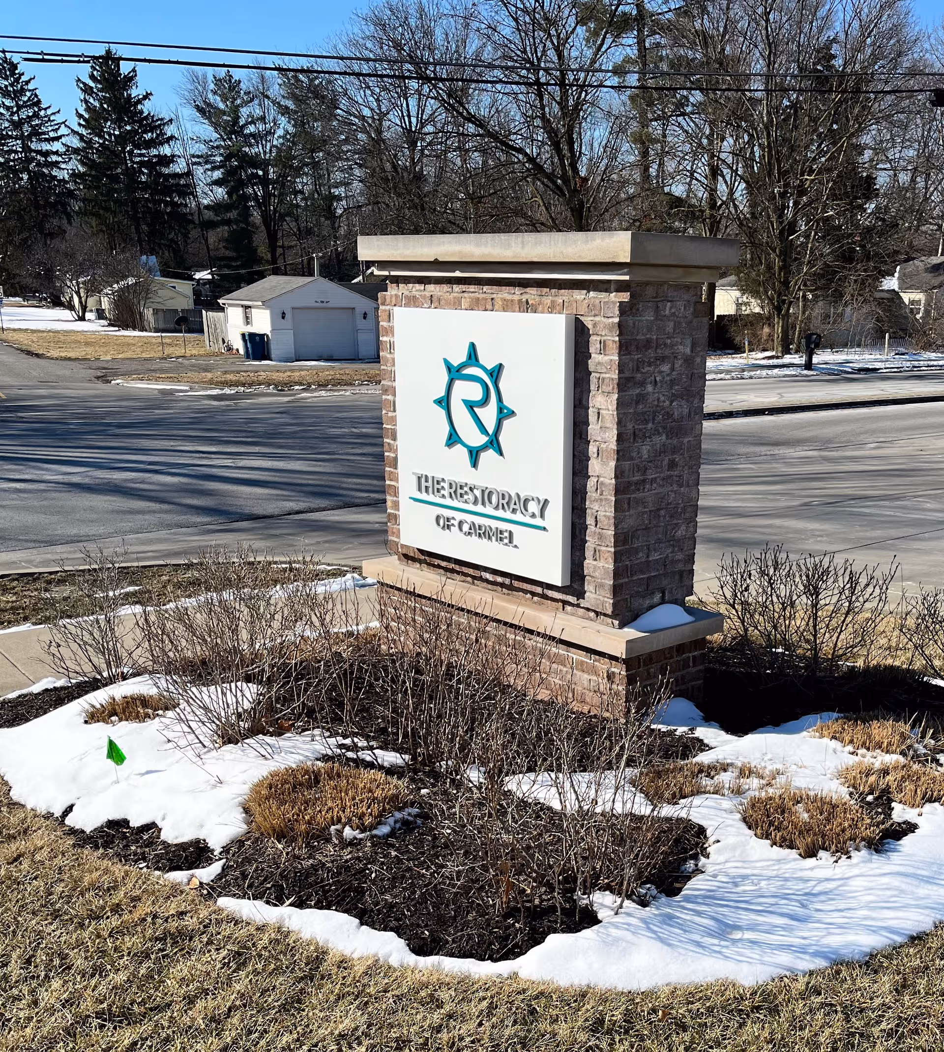 Exterior brick sign monument with The Restoracy of Carmel at snowy front lawn.