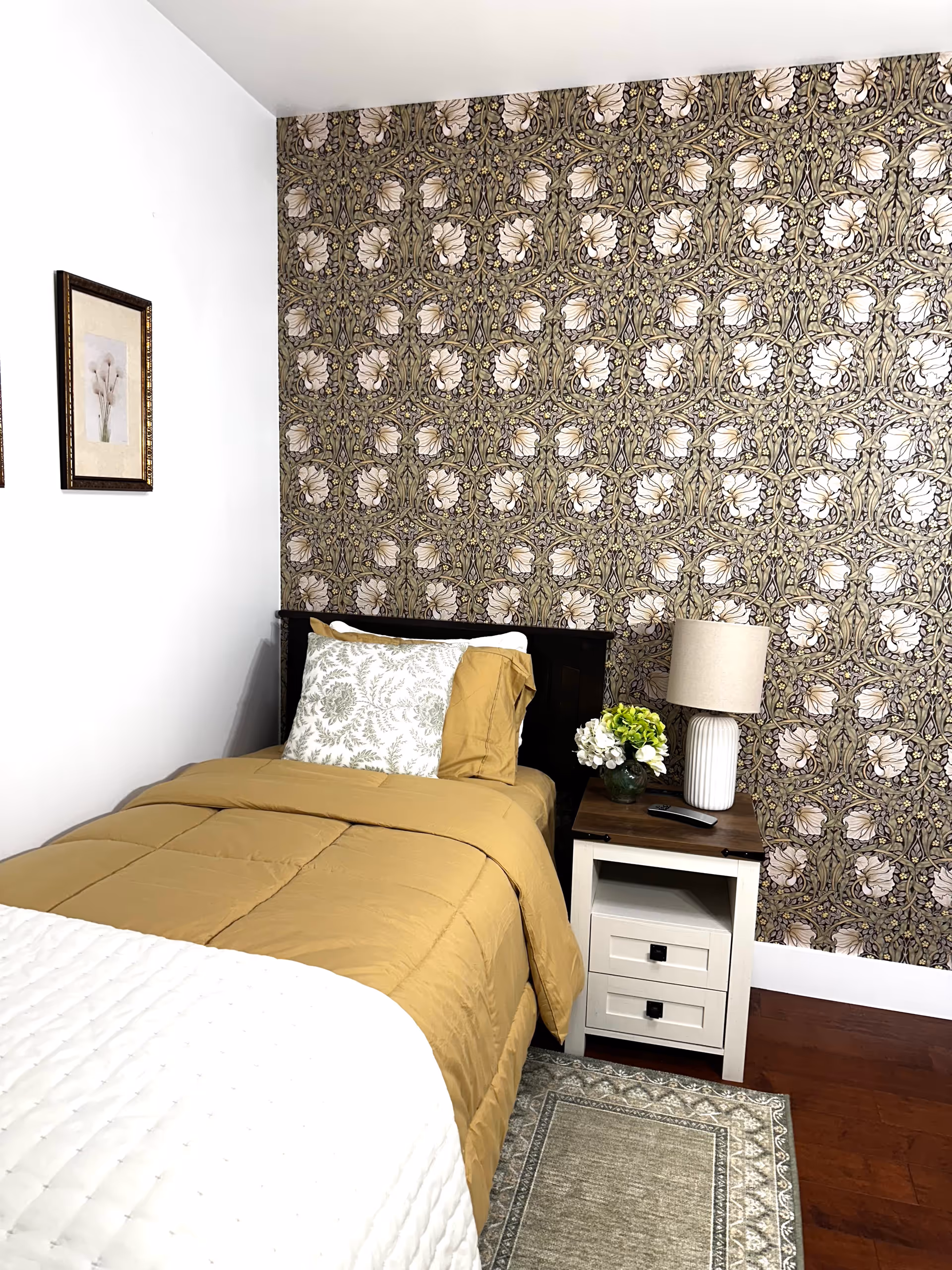 Cozy bedroom with patterned wallpaper, single bed, nightstand, lamp, and decorative accents.