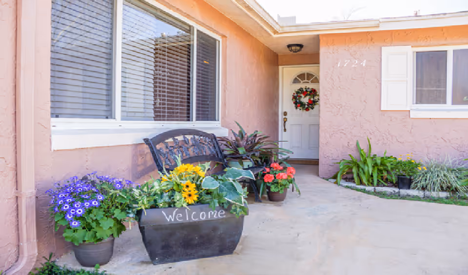 Entrance to a pink stucco assisted-living facility with bench and blooming planters.