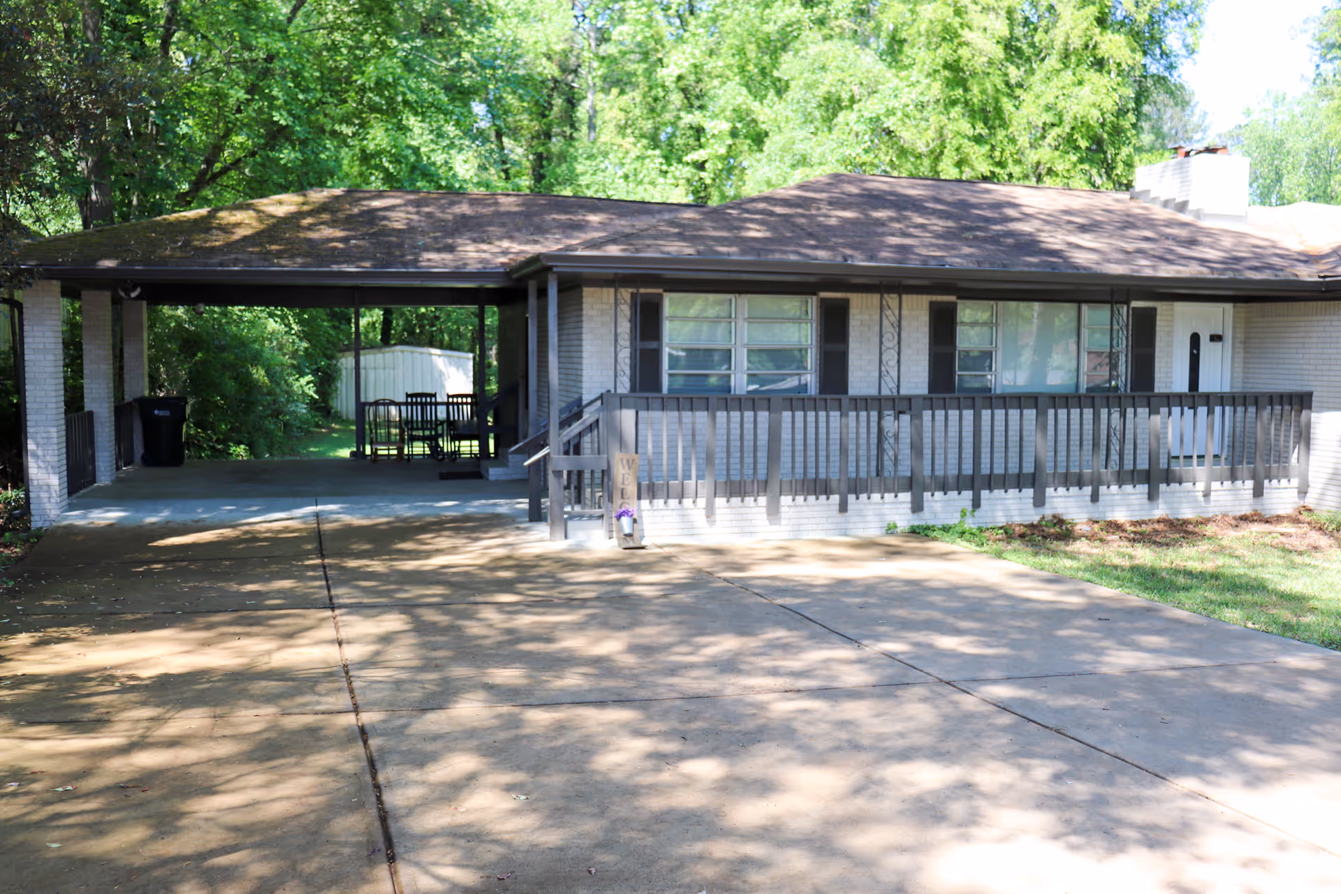 Single-story residence with front porch, railing, and carport amid shady trees.