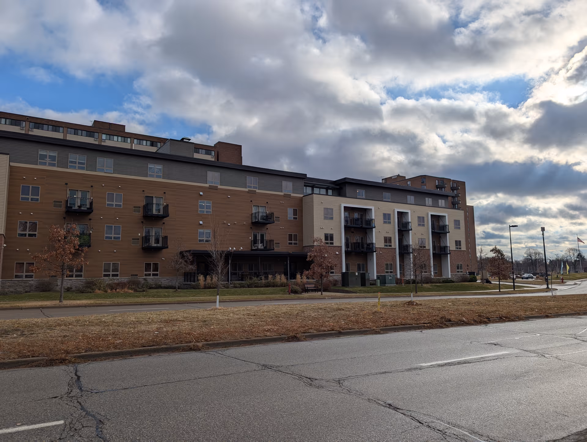 Front exterior of a multi-story senior living building with balconies under a cloudy sky.